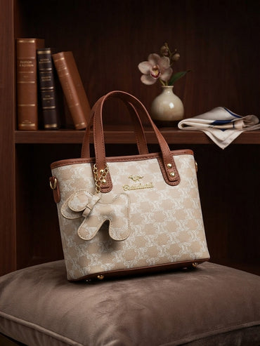 Beige monogram print structured tote bag with tan handles and plush animal charm