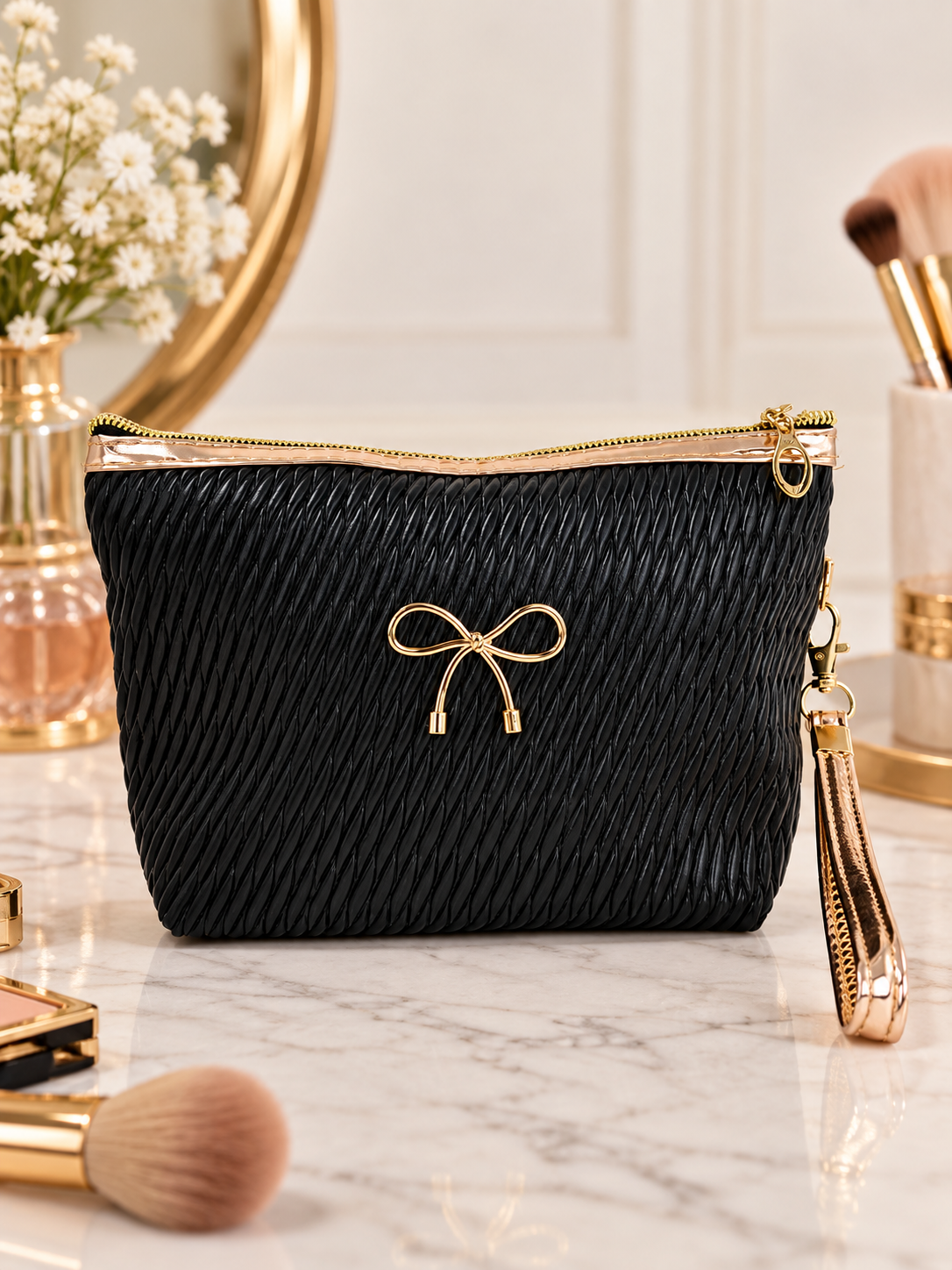 Black quilted cosmetic pouch with gold bow emblem and wristlet strap, zip closure