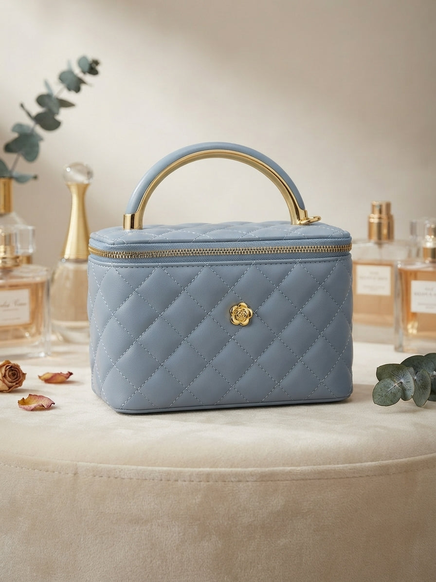 Blue quilted vanity cosmetic case with metal handle, gold emblem, and zip closure