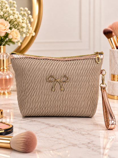 Beige pleated quilted cosmetic pouch with gold bow accent, zip top, and wristlet strap