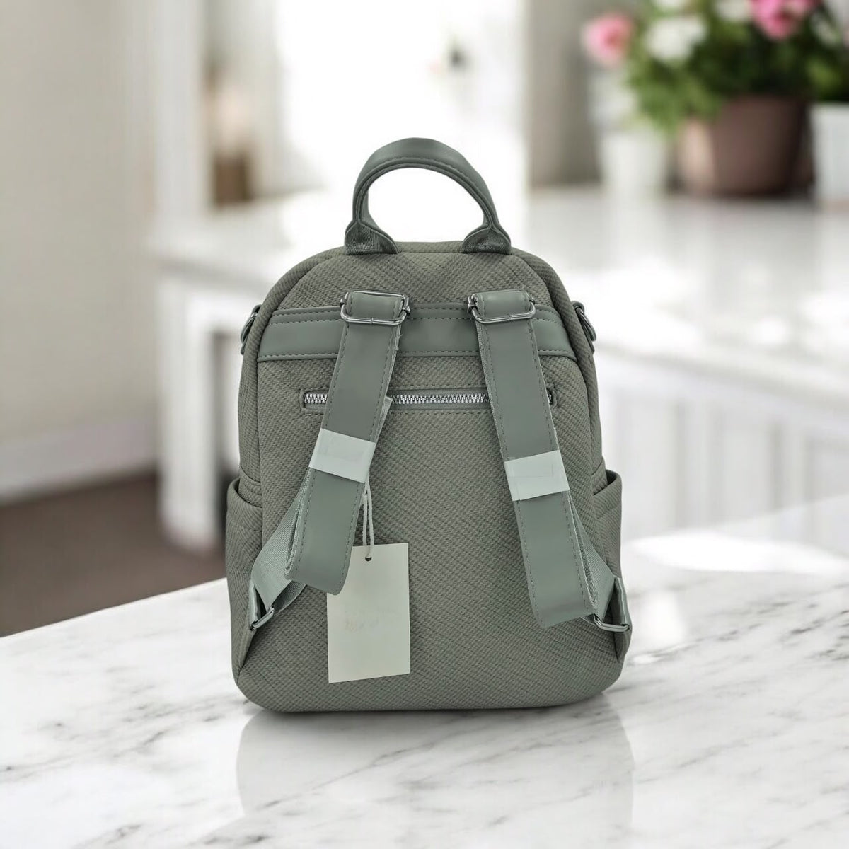 Grey textured mini backpack with top handle, twin front straps, and front pocket zipper