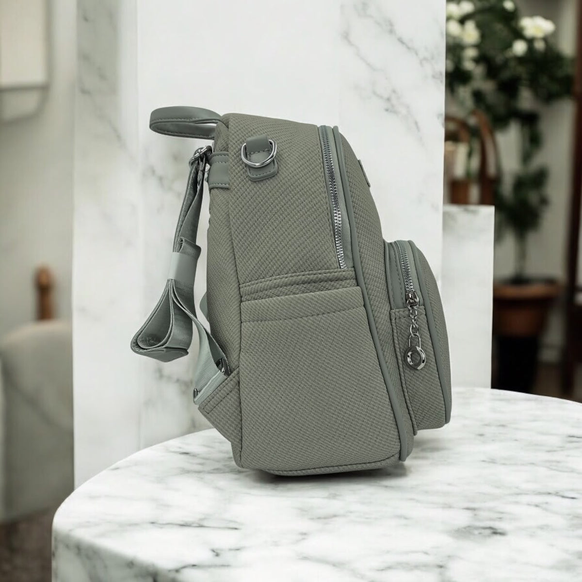Grey textured backpack shown from side with zipper front pocket and adjustable shoulder strap