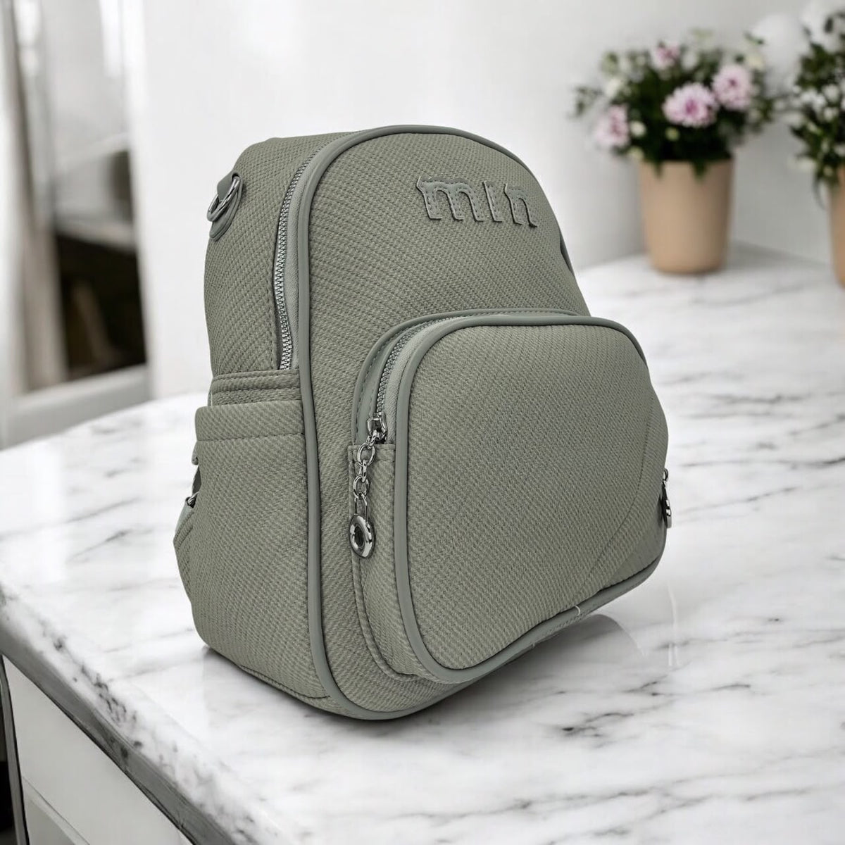Grey textured backpack with front zipper pocket, chain pull, and embroidered logo