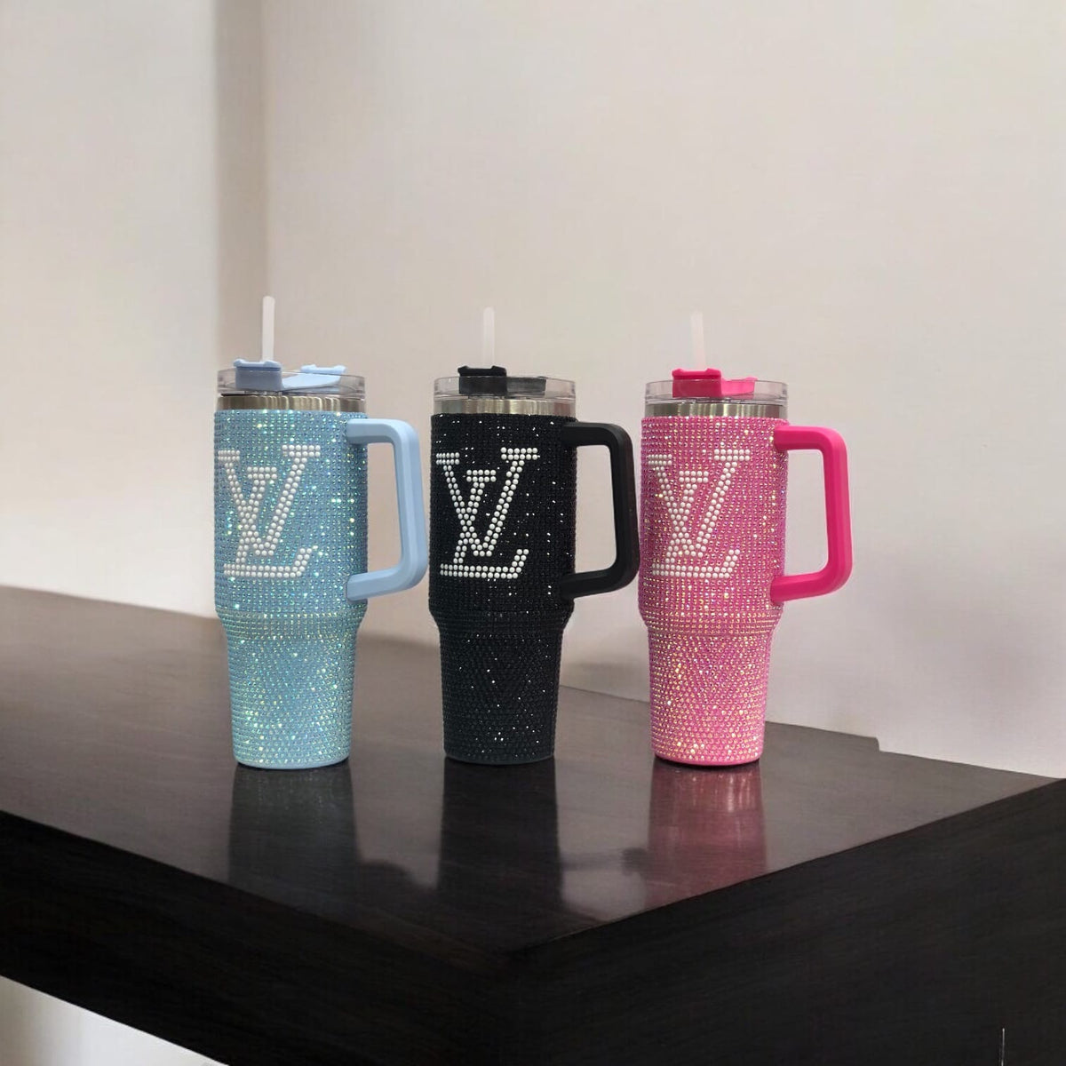 Three rhinestone LV tumblers: teal, black, and pink, each with handle and clear straw