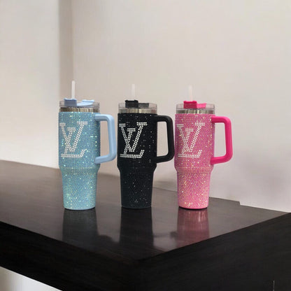 Three rhinestone LV tumblers: teal, black, and pink, each with handle and clear straw