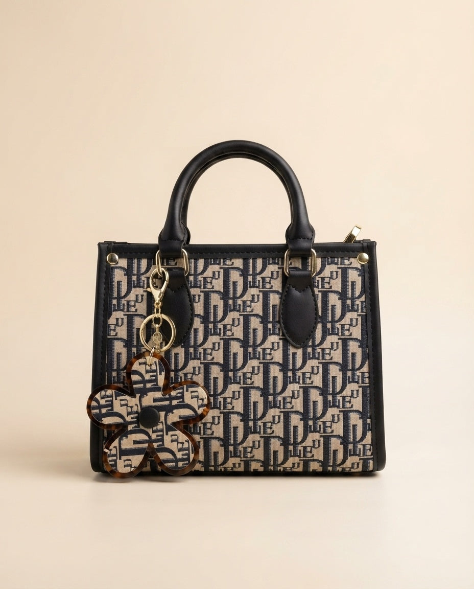 Structured tote bag with navy-and-black logo print, top handles, and tortoiseshell-style flower charm
