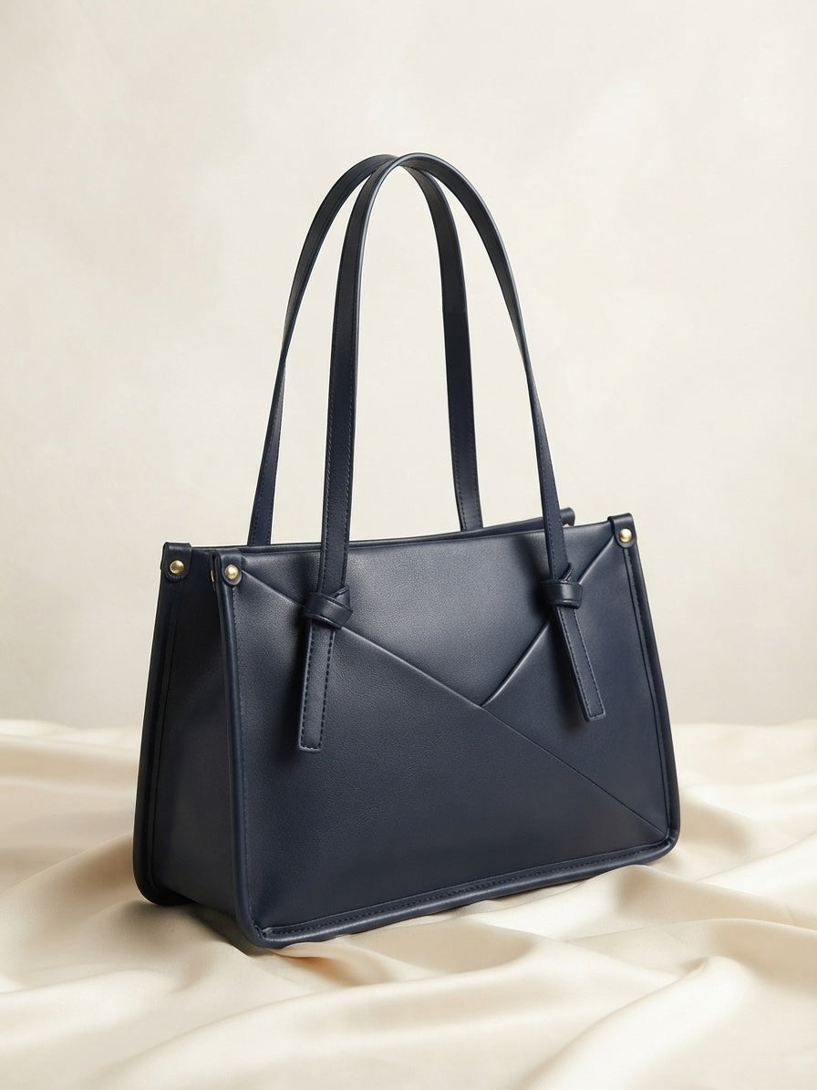 Knot-accent structured shoulder bag in navy with top handles, diagonal seam, and gold studs