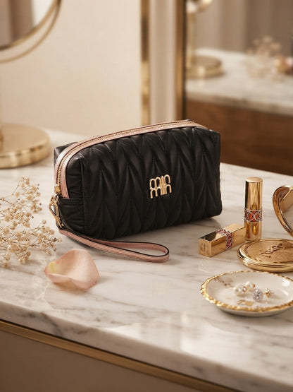 Black quilted cosmetic pouch with wristlet strap and gold logo, gold zipper pull