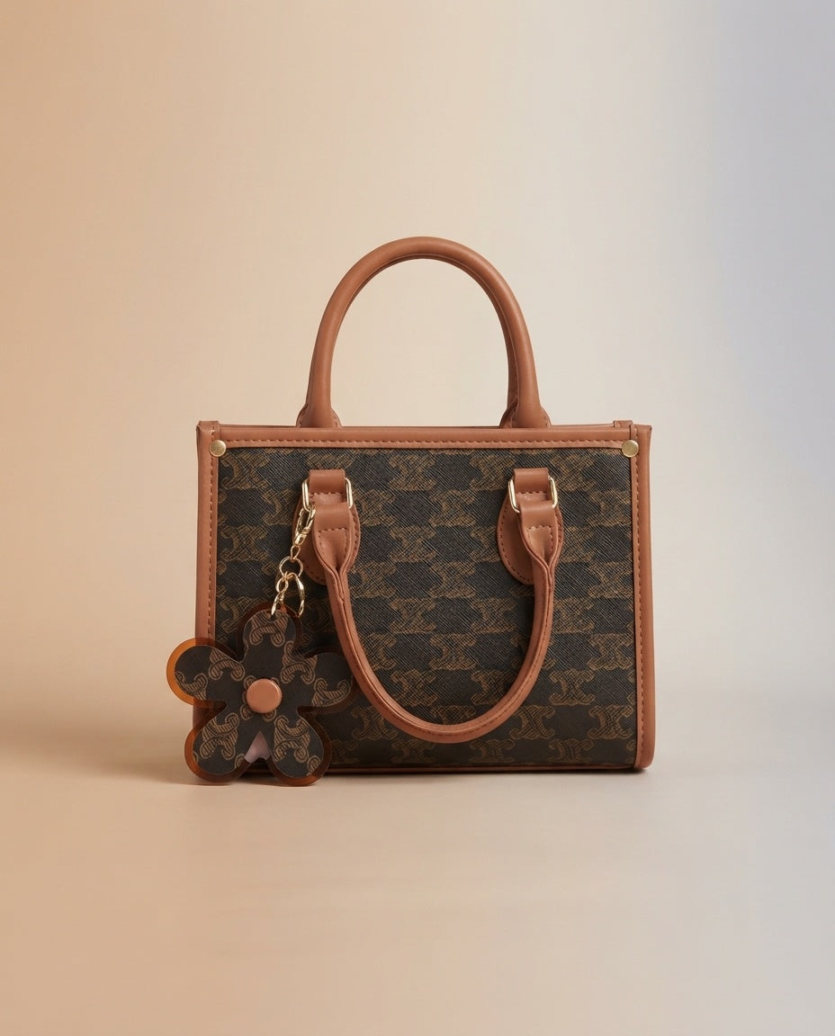 Structured tote bag in brown pattern with tan handles, flower charm, and crossbody strap
