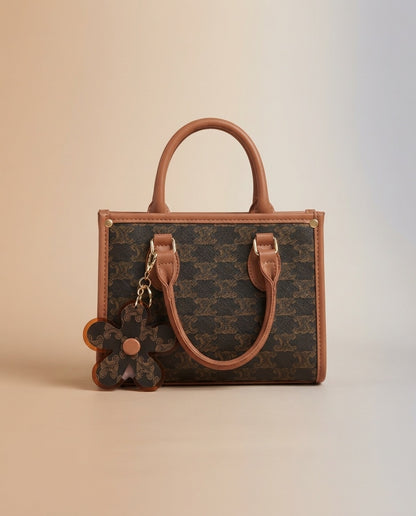 Structured tote bag in brown pattern with tan handles, flower charm, and crossbody strap