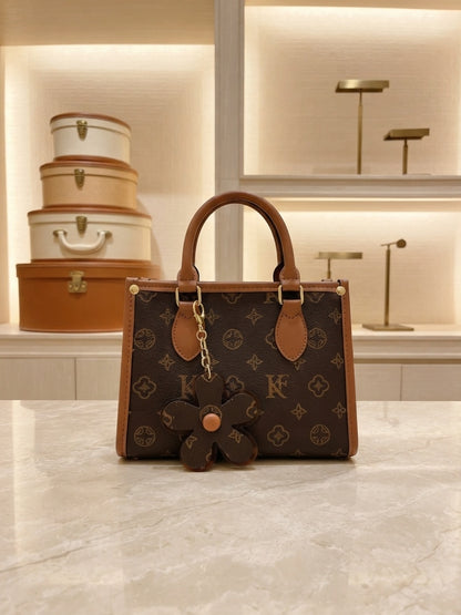 Structured monogram tote bag with top handles, crossbody strap, and flower charm