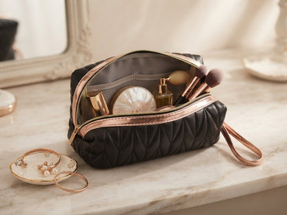 Black quilted cosmetic pouch open with wristlet strap and gold logo, showing contents