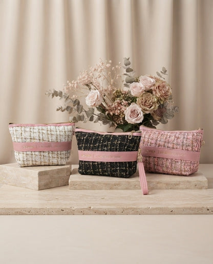 Tweed cosmetic pouch set with wristlet straps in pink, black, and beige, on display