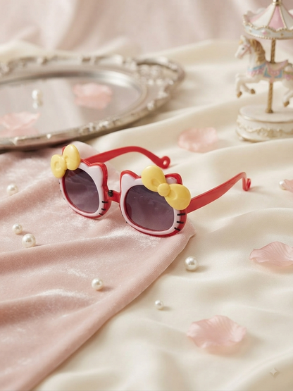 Kids cat-style sunglasses with dark lenses, red frame, and yellow bow accents