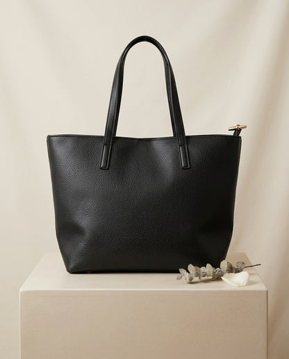 Pebbled faux leather pocket tote bag in black with buckle strap handles and front pocket
